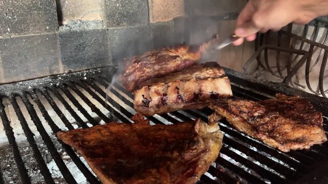 A grill master checks the succulent Argentinian ribs with a fork as they cook over hot coals at a traditional barbecue. Horizontal real footage
