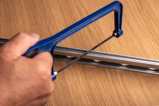 An used hacksaw with sawdust and a human hand is cutting a metall rail to get the right size.