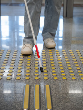 A blind woman walks on tactile paving. Close-up of her feet and a walking stick.