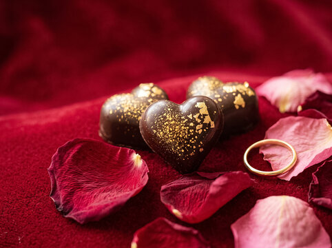 heart shaped chocolate candies with gold on red velvet with rose petals and a gold ring romantic composition