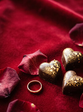 gold dusted chocolate hearts and red rose petals with a gold ring on a velvet background vertical frame