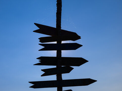 Silhouetted handmade direction signpost glowing in backlit evening sun.