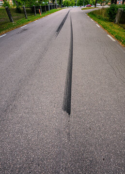Fresh black tire skid marks across quiet Swedish road.