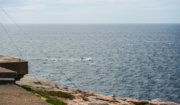 Small motorboat crossing open sea beside rocky Norwegian coast.