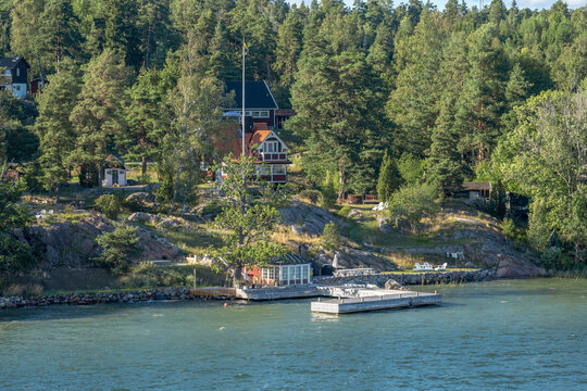 Red wooden house on rocky forested shoreline.