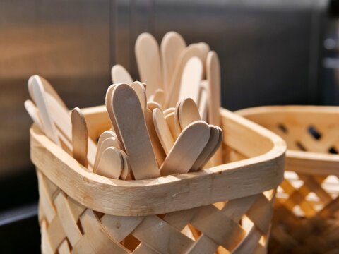 Disposable eco-friendly wooden coffee stirrers standing inside a woven bamboo basket on a cafe counter for sustainable beverage service.