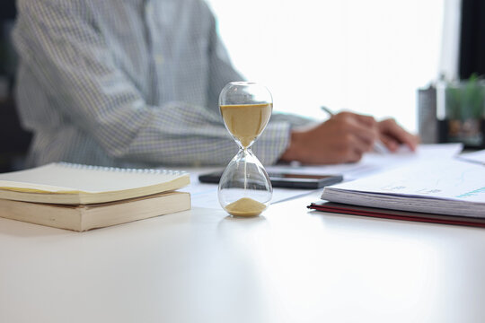 Businessman at a desk with an hourglass in the foreground, representing a time management concept.