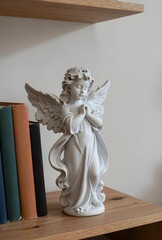 Obraz premium Spirituality and peace, small angel statue with praying hands standing on a wooden shelf next to vintage books for home decor and religious inspiration