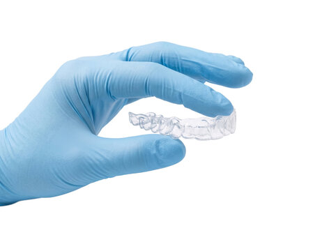 Dentist hand in blue surgical glove holding a transparent dental teeth aligner against a transparent background