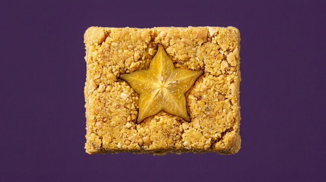 Peanut candy square topped with starfruit slice on purple background