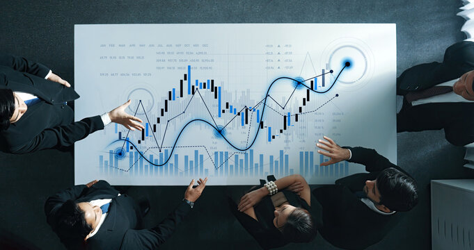 A group of business professionals reviews financial data on a large screen, showcasing a detailed analysis of stock market trends and investment strategies. Scalp