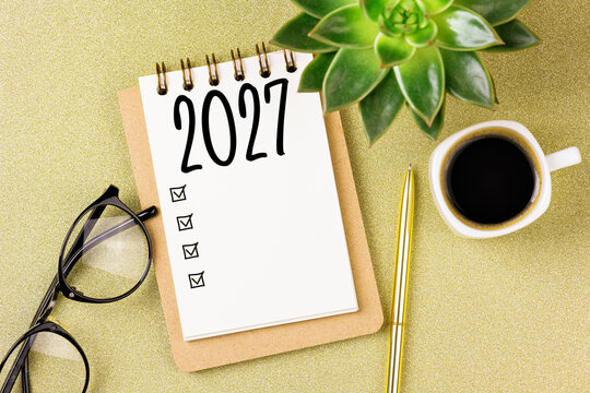 2027 New year resolutions on desk. 2027 goals list with notebook, coffee cup, plant on golden background. Resolutions, plan, goals, action, checklist, idea concept. New Year 2027 resolutions
