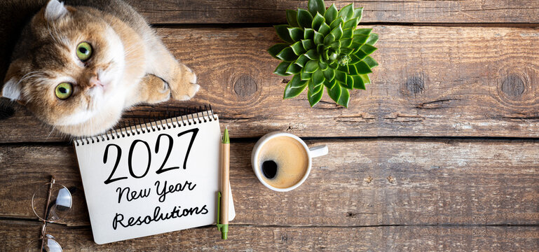 New year resolutions 2027 on desk. 2027 resolutions list with notebook, coffee cup, cute cat on table. Goals, resolutions, plan, cozy, hygge concept. New Year 2027 template, copy space