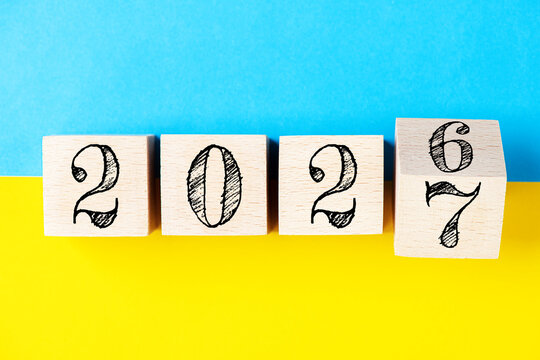 2027 Happy new year concept. Flipping of wooden cube block change from 2026 to 2027 on yellow and blue background ukrainian flag. Politics, support for Ukraine, business, inspiration to success ideas