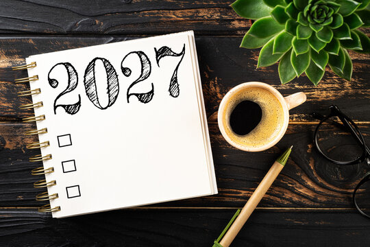New year resolutions 2027 on desk. 2027 goals list with notebook, coffee cup, plant on wooden table. Resolutions, plan, goals, action, checklist, idea concept. New Year 2027 resolutions. Copy space