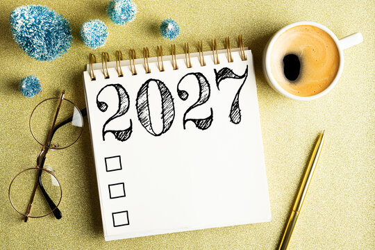 2027 New year resolutions on desk. 2027 goals list with notebook, coffee cup, festive decorations on golden background. Resolutions, plan, goals, checklist, idea concept. New Year 2027 resolutions