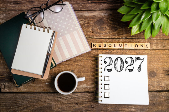 New year resolutions 2027 on desk. 2027 goals list with notebook, coffee cup, plant on wooden table. Resolutions, plan, goals, action, checklist, idea concept. New Year 2027 resolutions, copy space