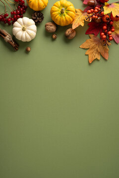 Autumn arrangement with mini pumpkins, colorful leaves, nuts and cinnamon on vertical green background for Thanksgiving