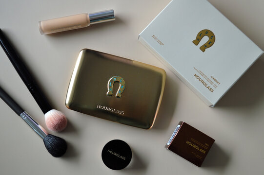 Luxury makeup flat lay featuring a shimmering gold compact, cream foundation, blush brushes, and cosmetic boxes arranged neatly on a soft neutral background