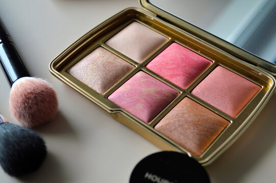 Luxury gold compact makeup palette with marbled pink and bronze blush shades displayed beside soft cosmetic brushes on a neutral vanity surface