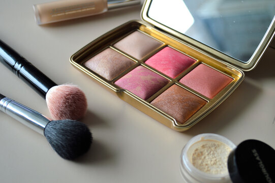 Elegant gold makeup palette with blush and highlighter shades displayed beside soft cosmetic brushes and loose powder on a bright vanity surface