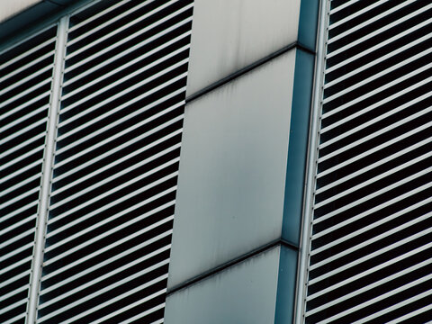 Diagonal striped metal louvers with vertical corner panel, modern architectural facade detail in monochrome teal tones