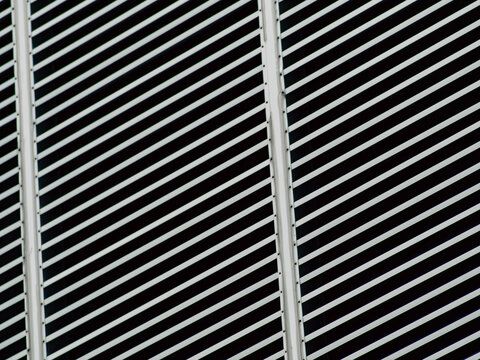 Diagonal striped metal louvers with vertical corner panel, modern architectural facade detail in monochrome teal tones