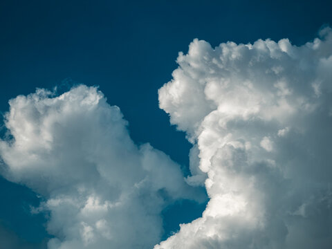 Two billowing white cumulus clouds against deep blue sky, dramatic natural weather formation background with bold contrast