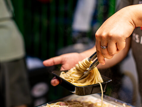 Vendor Pouring Creamy Sauce Over Spaghetti in Takeaway Box Street Food