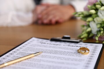 Obraz premium Marriage contract, wedding rings and couple at wooden table, selective focus