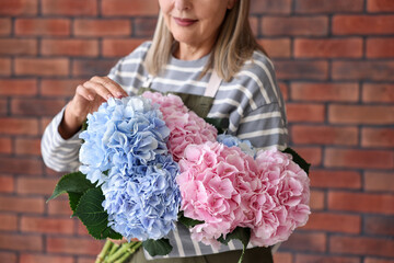Fototapeta premium Florist with bouquet of beautiful hortensia flowers near brick wall, closeup