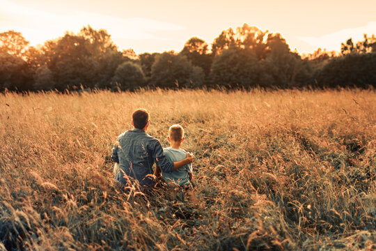 Father and son sitting together watching nature sunset, fatherhood, family love, parenting, support and childhood bonding concept
