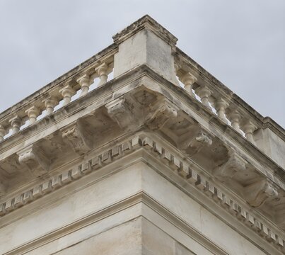Limestone cornice with dentils and a carved balustrade on a corner block with chipped cream stone