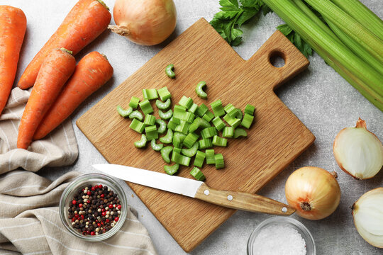 Cut celery stalks, carrots, onion bulbs and spices on grey table, flat lay