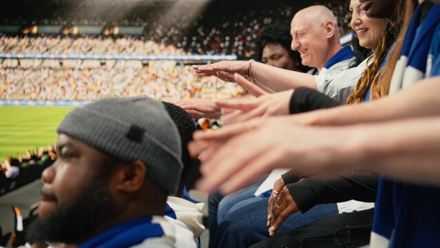 Women supporters of the blue team cheer with raised arms in stadium stands as a capo energizes the crowd with a megaphone during a live soccer match, celebrating goals and football fan culture.
