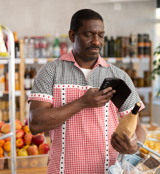 African man in store scans QR code on wine bottle. With help of mobile app, buyer receives information about wine beverage product. He checks manufacturers data in registry database of national agency
