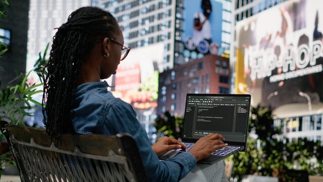 Woman software developer writes code on laptop at park bench