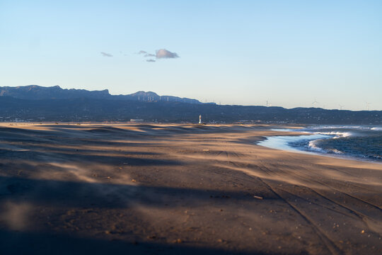 Lighthouse on Ebro Delta Dunes at Sunset with Mountains and Wind Turbines