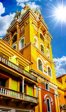 Vibrant yellow colonial church tower against a bright blue sky with sunburst. Historic architecture in Cartagena, Colombia.