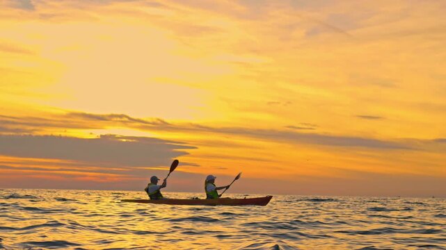 A couple kayaks during a stunning sunset, embracing an active lifestyle and adventure. Their synchronized paddling in the serene ocean represents a recreational pursuit and memorable vacations.