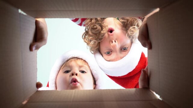 Happy children are unpacking a Christmas gift box. Kids dressed in Xmas pajamas are having fun at home. Slow motion