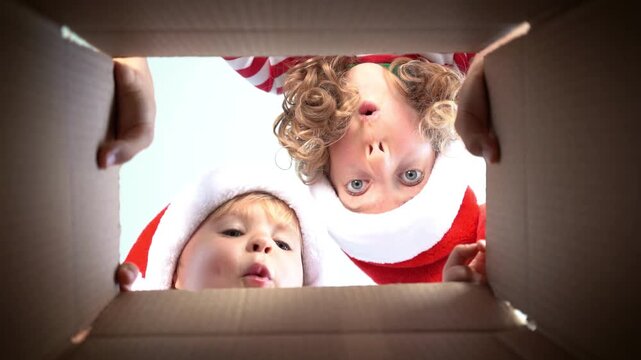 Happy children are unpacking a Christmas gift box. Kids dressed in Xmas pajamas are having fun at home. Slow motion