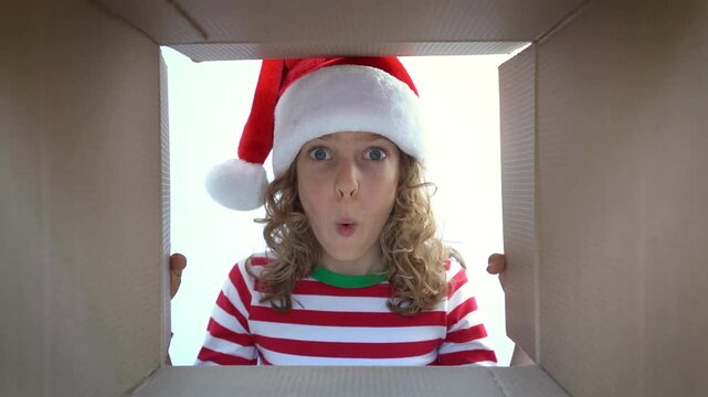 Happy child is unpacking a Christmas gift box. Girl dressed in Xmas pajamas is having fun at home. Slow motion