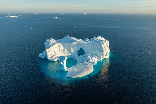 Aerial view of an arch iceberg floating in the deep blue waters of the Arctic Ocean, surrounded by smaller ice fragments in Greenland.
