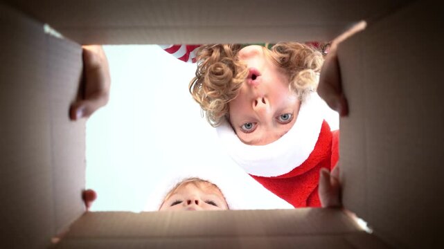 Happy children are unpacking a Christmas gift box. Kids dressed in Xmas pajamas are having fun at home. Slow motion