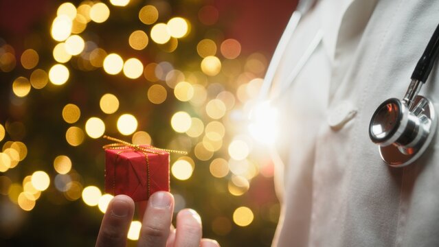 Cardiologist Doctor Gives Small Red Christmas Gift in Front of Flashing Tree