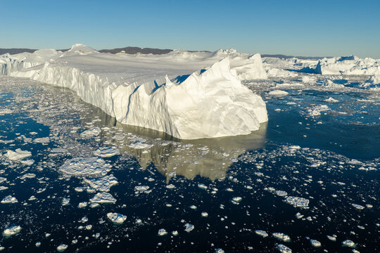 Aerial view of a massive iceberg from the Ilulissat glacier floating in the deep blue waters of Disko Bay with scattered ice fragments under a clear sky Greenland.