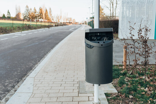 One street metal trash can on a pole on a city street on a winter day.