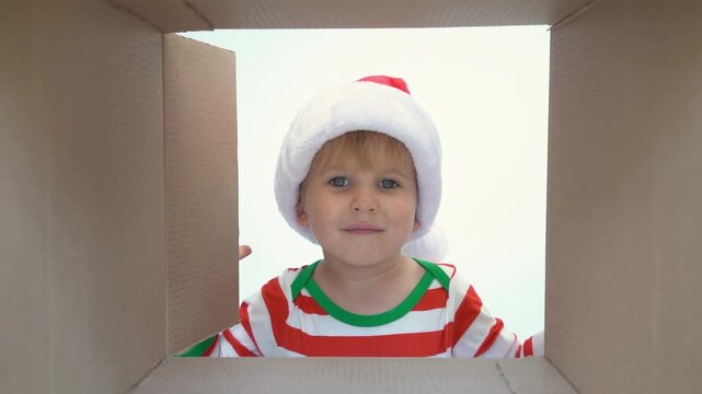 Happy child is unpacking a Christmas gift box. Kid dressed in Xmas pajamas is having fun at home. Slow motion