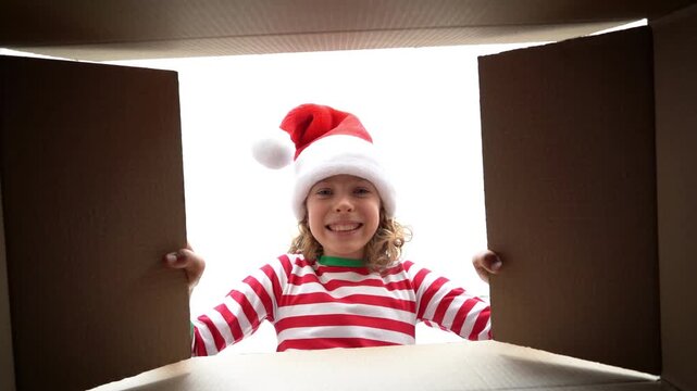 Happy child is unpacking a Christmas gift box. Girl dressed in Xmas pajamas is having fun at home. Slow motion